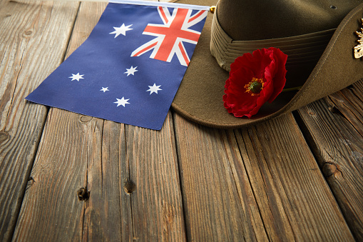 Anzac army slouch hat with Australian Flag and Poppy on wooden background.