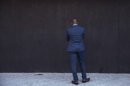 Rear view of businessman thinking against grey wall