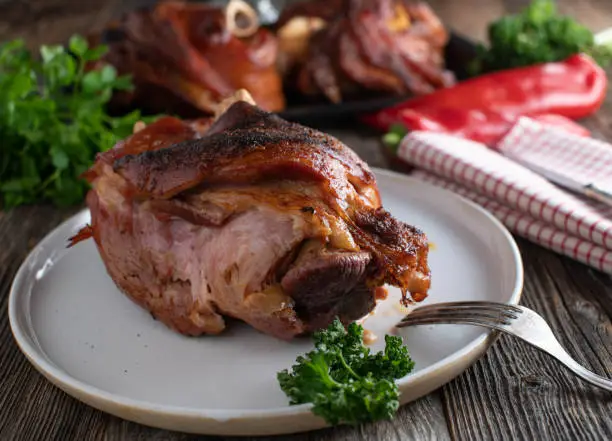 Traditional german meat dish with ham hock or pork knuckle fresh oven baked and served on a plate on rustic and wooden table background. Closeup and front view