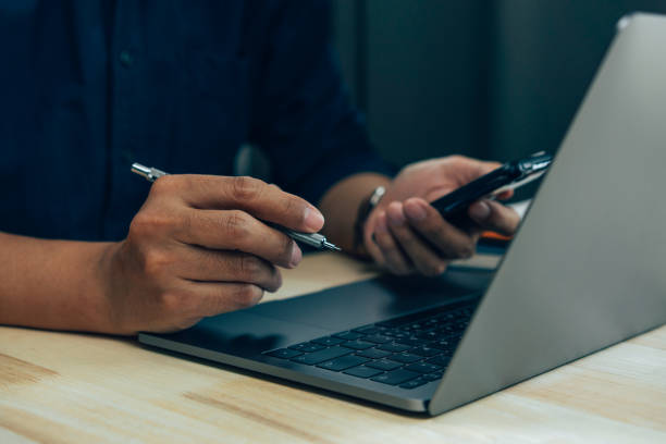 istock Businessman hand using laptop and smart phone working at home office. 1383386634