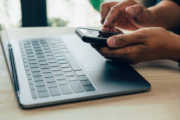 istock Businessman hand using laptop and smart phone working at home office. 1383386806