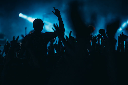 Young man with raised hands having fun while listening music performance in a concert crowd on a music festival. Nightlife and music entertainment concept.