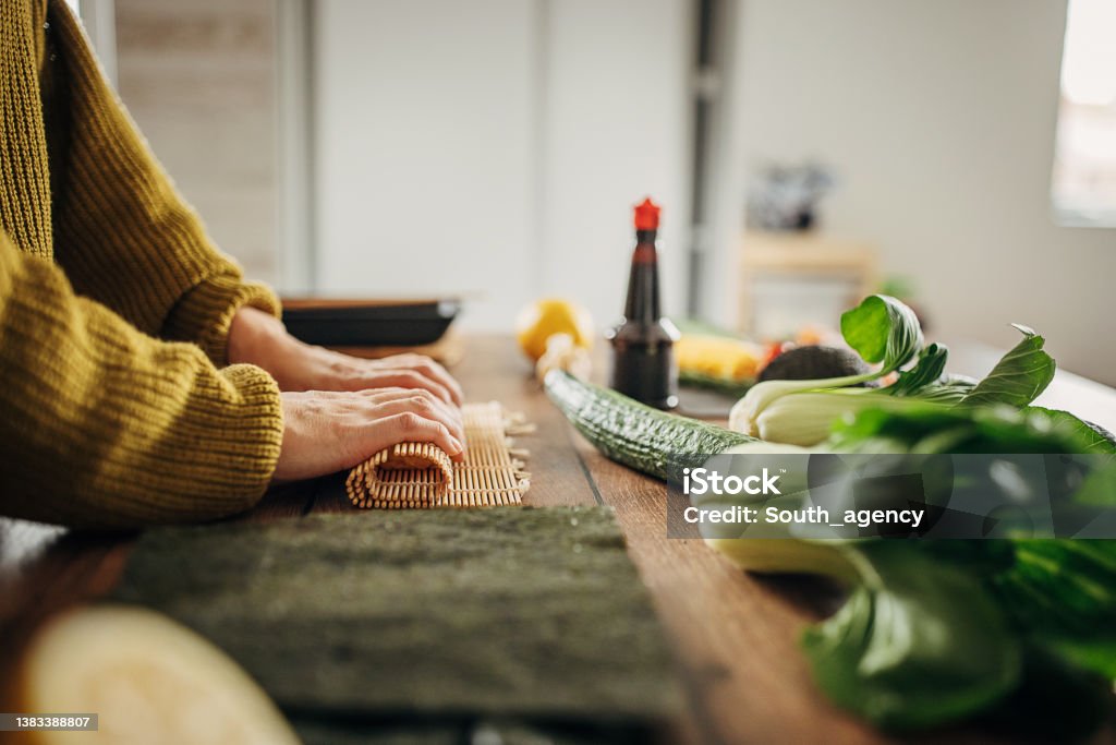 Woman making sushi One woman, modern Japanese female preparing sushi in kitchen at home. Rolling Stock Photo