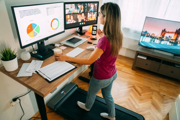 Woman at standing desk home office talking on business video call Woman working from home at standing desk is walking on under desk treadmill working at home stock pictures, royalty-free photos & images