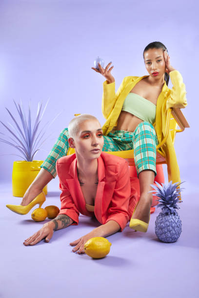 Full length shot portrait of two attractive young women dressed in funky attire against a purple background Put the YOU back in unique haute couture stock pictures, royalty-free photos & images