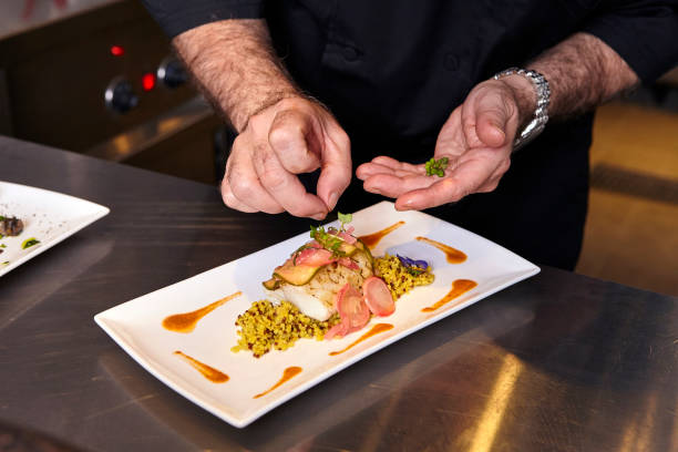 Chef adds the final touch to a grilled sea bass steak, red lentils  with candied radits and edible flowers