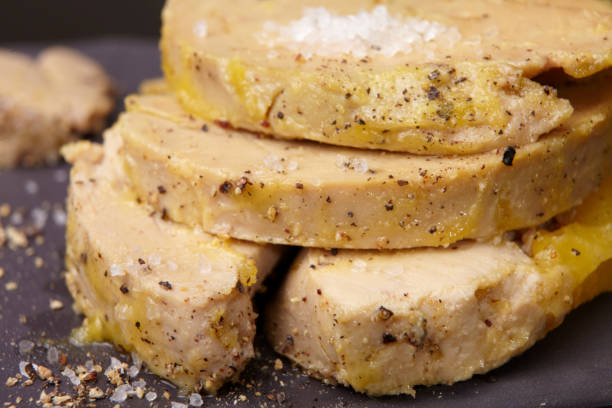 Slices of semi-cooked foie gras Close-up of three slices of semi-cooked foie gras layered and covered with fresh ground black pepper and Guérande salt. Another slice is laid out blurred in the background. foie gras stock pictures, royalty-free photos & images