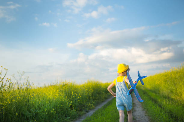 une fille portant un chapeau panama jaune lance un avion jouet dans le champ. l’été, l’enfance heureuse, les rêves et l’insouciance. tour aérien d’une agence de voyages en voyage, vol, aventure et vacances. - fighter plane photos et images de collection