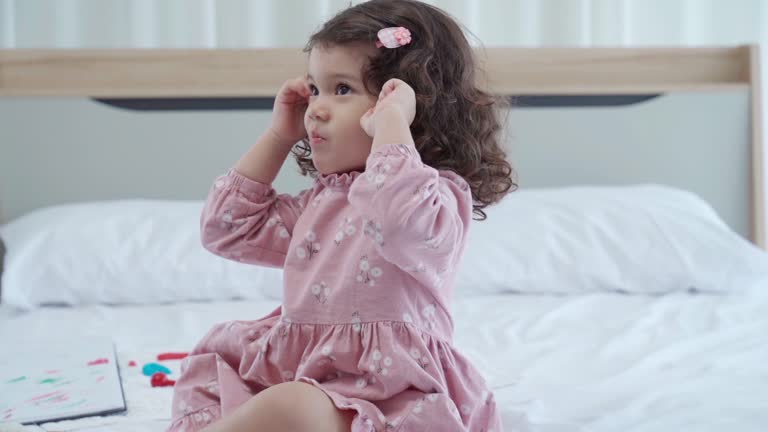 Facial expression by curly hair girl sitting on bed  and used fingers on ears for silance  gesturing  tantrum child , Taming a Tantrum , displeasde emotion