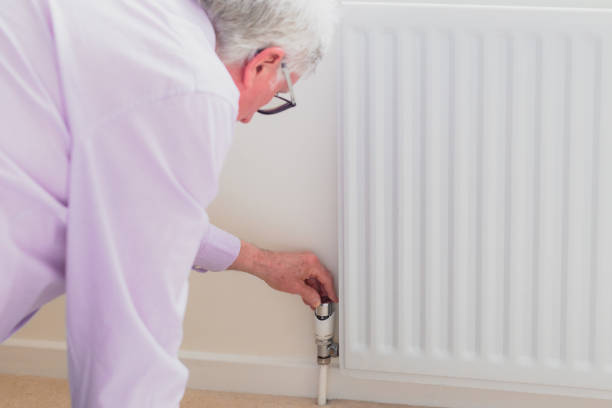 istock Senior man adjusting heat on radiator - reducing energy consumption 1383421142