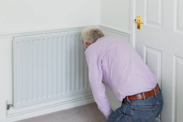 istock Senior man adjusting heat on radiator - reducing energy consumption 1383421171