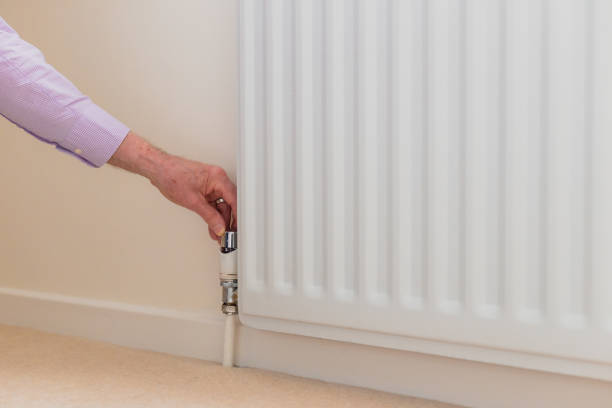 istock Senior man adjusting heat on radiator - reducing energy consumption 1383421183