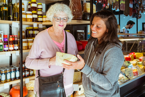 Senior woman buying cheese with female caregiver at store.
