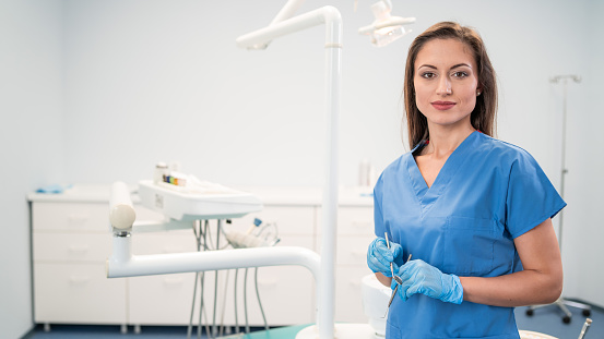 Portrait of female dentist,holding dental tool and standing at her office