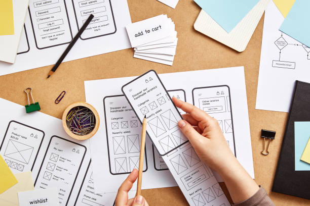 UX designer planning application for mobile phone UI / UX front end designer working on mobile responsive website. Flat lay image of several app wireframe sketches over product designer desk. user experience stock pictures, royalty-free photos & images
