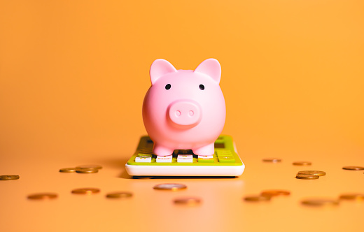 Una alcancía sobre una calculadora verde con monedas dispersas aisladas sobre fondo naranja en fotografía de estudio. Conceptos de ahorro de dinero, finanzas e inversiones. photo