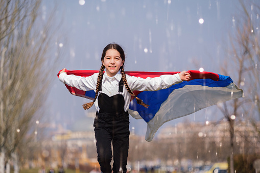 Happy Ukrainian girl running at the park waving the yellow and blue national flag. Concept of love for Ukraine. Independence, flag, Constitution Day of Ukraine
