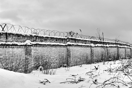 An old but still very strong brick fence, barbed wire is stretched over the fence, snow, a simple landscape