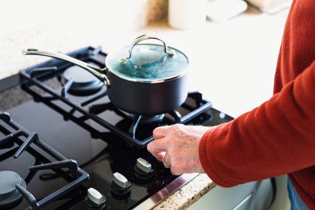 A senior man turning down the heat, and saving energy, on his gas hob in the kitchen at home. Room for copy space.