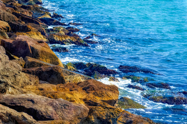 Foamy Mediterranean sea hitting rocky shore during hot summer day.