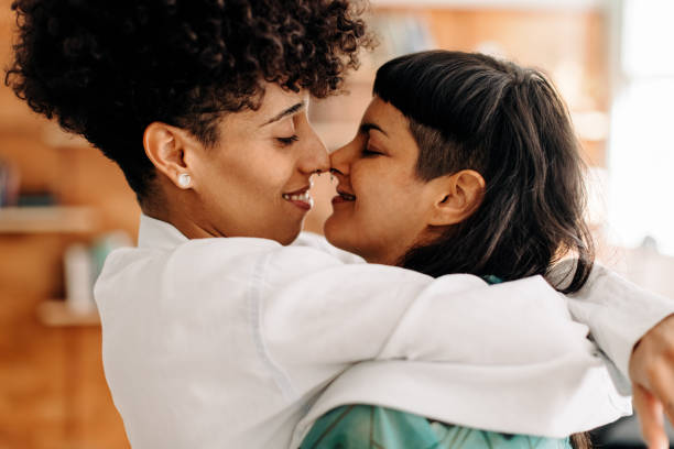 Flirty lesbian couple touching their noses Flirty lesbian couple touching their noses together. Two romantic female lovers smiling cheerfully while embracing each other. Affectionate young LGBTQ+ couple bonding at home. kissing stock pictures, royalty-free photos & images