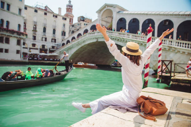 frau, die in der nähe der rialtobrücke in venedig italien sitzt und mit gondeln auf den canal grande blickt - venice italy italy rialto bridge italian culture stock-fotos und bilder