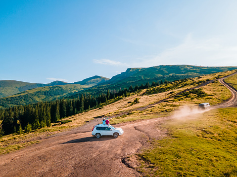 aerial view of couple sitting on the suv car roof enjoying view of carpathian mountains Ukraine