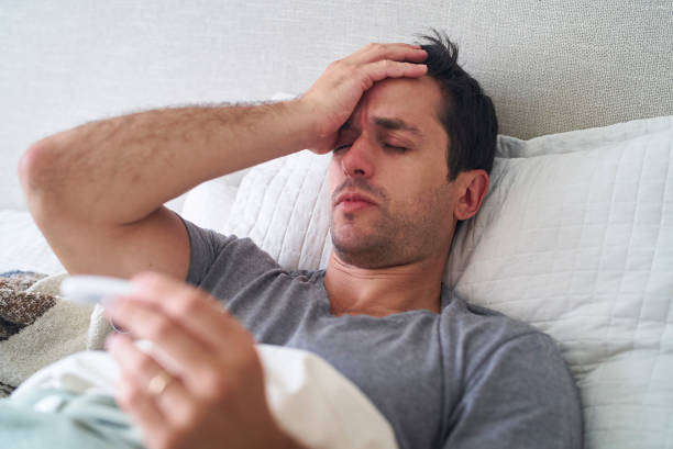 istock Sick hispanic adult man feeling unwell while lying in bed holding digital thermometer 1383469004
