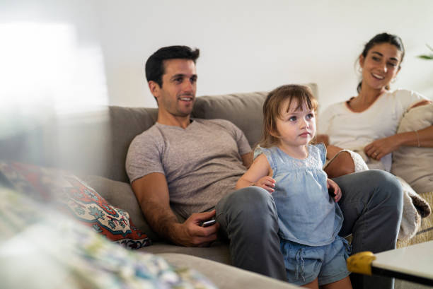 istock Young adult couple watching tv with toddler while sitting on sofa 1383473242