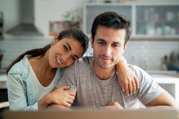 istock Hispanic straight couple embracing each other while having a video conference on laptop 1383473323