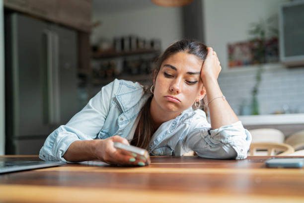 bored young adult hispanic woman looking at smart phone while leaning on hand - 無聊 個照片及圖片檔