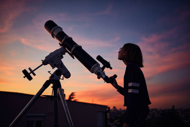 istock Girl with astronomical telescope stargazing under twilight sky. 1383473880