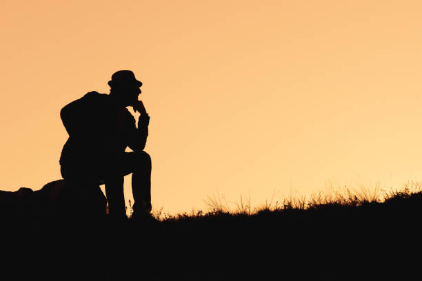 silhouette of a thinking man sitting on a stone. pose of a thinker in a hat
