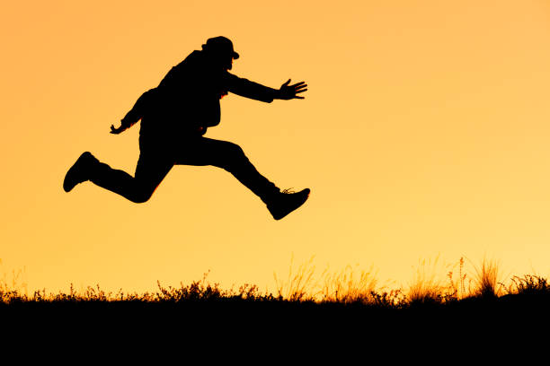 silhouette of a man in a hat while running and jumping on an orange background. running from the problems of people from the city to nature outdoors