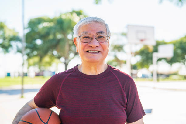 istock Cheerful asian american senior man holding ball while looking at the camera 1383476138