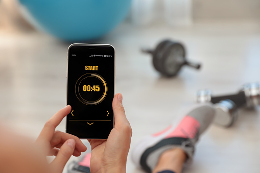 Young woman using fitness app on smartphone indoors, closeup. Space for text