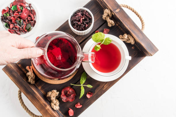 tee ceremonia . die hand einer frau gießt duftenden roten hibiskustee in eine tasse minzblätter. draufsicht auf das holztablett mit morgentee. - mint tea lemon tea leaves glass stock-fotos und bilder