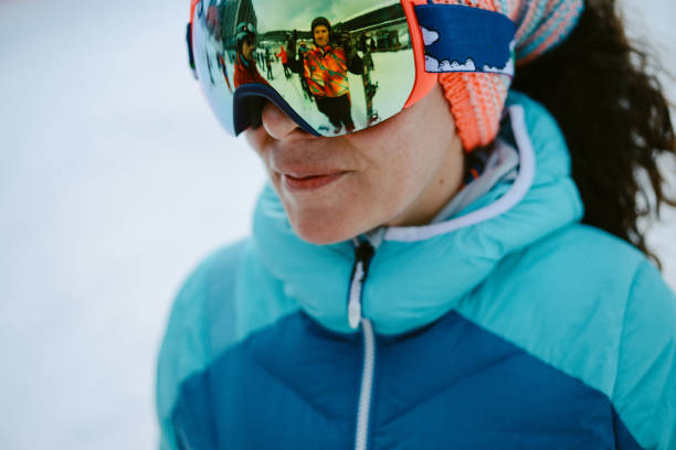 Close up of the ski goggles of a man with the reflection of snowed mountains.  A mountain range reflected in the ski mask.  Man  on the background blue sky. Wearing ski glasses. Winter Sports.