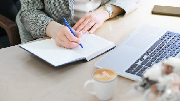 istock woman in formal clothes making notes in a diary, planning a day or week. female hands on a working table with laptop and coffee cup. 1383488950