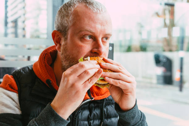 istock Man eating cheeseburger in fast food restaurant 1383489948