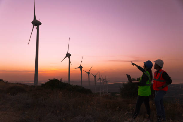 istock Young maintenance engineer team working in wind turbine farm at sunset. 1383490830