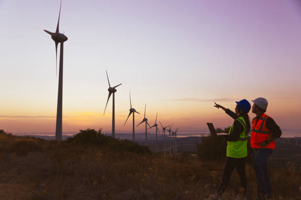istock Young maintenance engineer team working in wind turbine farm at sunset. 1383490870