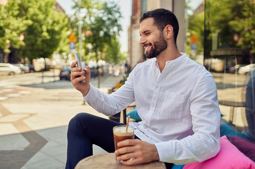 Smiling man using smartphone during coffee break outside a coffee shop in the city