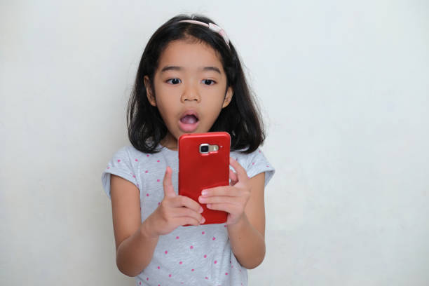 Asian kid showing shocked face expression when looking to his mobile phone Asian kid showing shocked face expression when looking to his mobile phone keluarga stock pictures, royalty-free photos & images