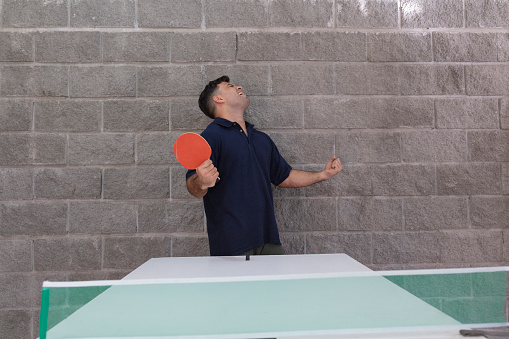 A male business executive regrets missing a shot during a ping-pong tennis match at a leisure room