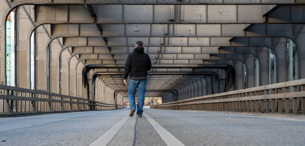 istock Man walking alone on a empty bridge above the river Elbe in Hamburg, Germany. 1383495390