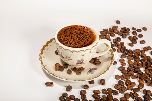 Cup of black coffee with scattered roasted coffee beans on white table. coffee concept