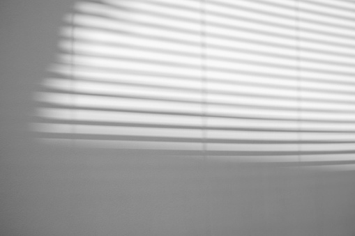 gray shadow of blinds windows overlay on the white wall background, sunlight through blinds, black and white