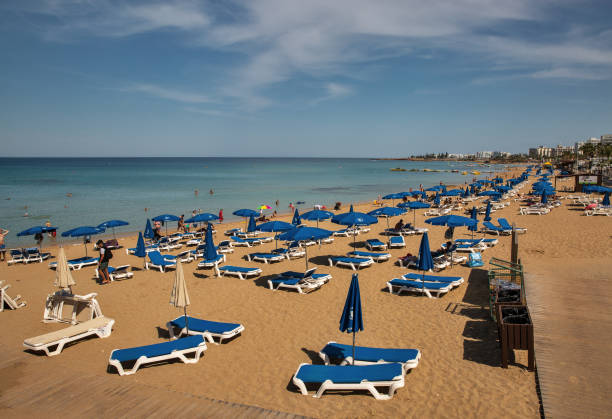 Protaras, Cyprus - May 25, 2021: People sunbath and relax at resort beaches with luxury hotels. Protaras has clear sky blue waters and sandy beaches, the most well-known of which is Fig Tree Bay.