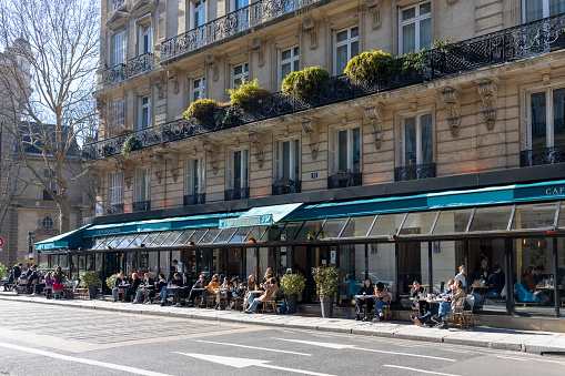 2022 Cafe terrace on the left bank of Paris, France. There are tourists and locals having a snack outside in the winter sunshine.